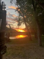 Sunset over a calm river, surrounded by trees, with a silhouetted net and bell in the foreground.